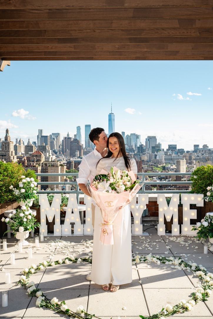 Jarryd kissing Leah's head as she holds a bouquet on the rooftop